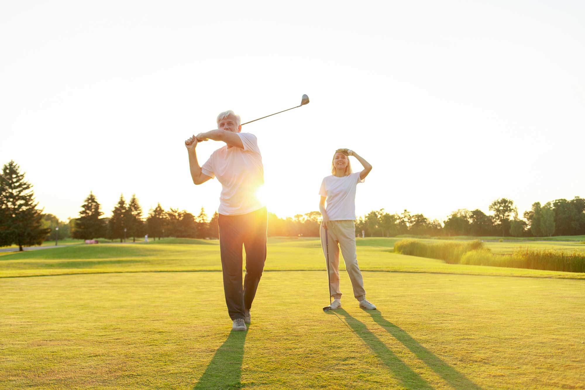 elderly senior couple in uniform playing golf on golf course at sunset